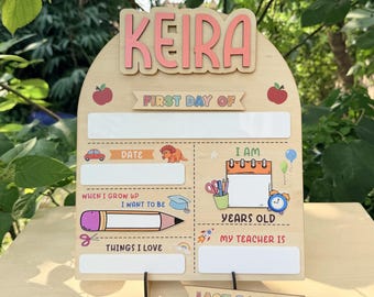 Può includere: Cartello in legno per il primo e l'ultimo giorno di scuola con il nome "KEIRA" in alto. Il cartello include spazi per la data, l'età, il nome dell'insegnante e altri dettagli, con illustrazioni colorate.
