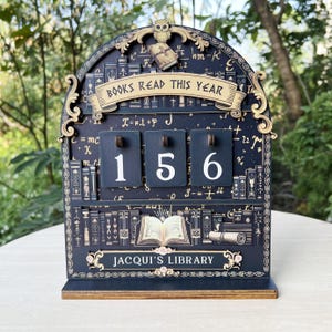 May include: A wooden book counter with the text "BOOKS READ THIS YEAR" and "JACQUI'S LIBRARY". The counter shows the number 156. The design features an owl, books, and mathematical symbols, in a dark blue and gold color scheme.