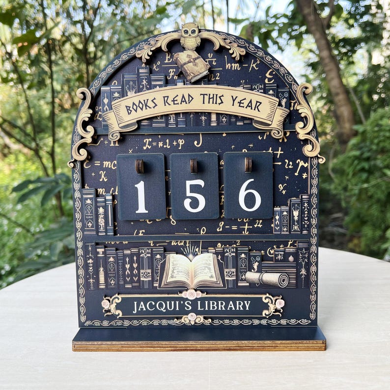 May include: A wooden book counter with the text "BOOKS READ THIS YEAR" and "JACQUI'S LIBRARY". The counter shows the number 156. The design features an owl, books, and mathematical symbols, in a dark blue and gold color scheme.
