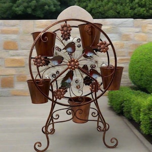 May include: A copper-coloured metal Ferris wheel planter with eight bucket-shaped pots. The wheel features bird and floral accents. The planter stands on a decorative base with scrolled feet, ideal for a garden or patio.