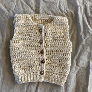 May include: A cream-colored crocheted vest with brown buttons.