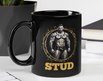 May include: Black coffee mug featuring a muscular man illustration within a gold dotted circle. The word "STUD" is printed in gold below the illustration. The mug has a black handle and a glossy finish.