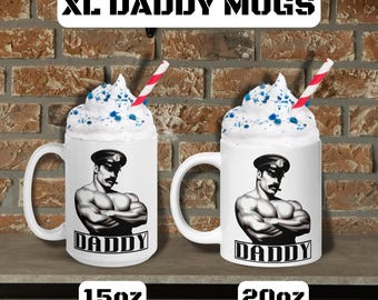 May include: Two white ceramic mugs with the text "XL DADDY MUGS". Each mug features a black and white illustration of a muscular man in a cap. The mugs are filled with whipped cream and a straw. One mug is labeled 15oz, the other 20oz.
