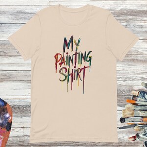 May include: A beige t-shirt with the text "MY PAINTING SHIRT" in colourful, dripping paint lettering.