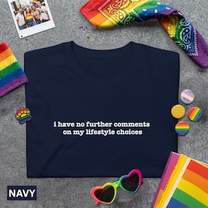 Peut inclure: T-shirt bleu marine avec le texte "i have no further comments on my lifestyle choices" en blanc. L'image comprend des accessoires sur le thème de l'arc-en-ciel, comme un bandana, des lunettes de soleil, des épingles et une petite photo, le tout sur une surface grise.