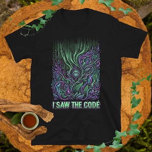 May include: Black t-shirt with a colourful graphic. The design includes an eye, flowing green and purple plant-like elements, and a matrix-style background. The text "I SAW THE CODE" is printed at the bottom of the design.