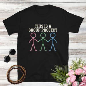 May include: Black t-shirt with the text "THIS IS A GROUP PROJECT" above a graphic of three stick figures holding hands. The stick figures are colored pink, green, and blue.