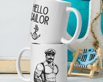 May include: Two white ceramic mugs with black text and illustrations. The top mug has the text "HELLO SAILOR" and an anchor. The bottom mug has a black and white illustration of a sailor with a mustache and a captain's hat.