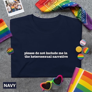 May include: A navy blue t-shirt with the white text "please do not include me in the heterosexual narrative". The image includes Pride-themed accessories such as a rainbow bandana, sunglasses, and pins.