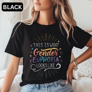 Könnte beinhalten: Schwarzes T-Shirt mit dem Text "THIS IS WHAT Gender EUPHORIA LOOKS LIKE" in farbenfroher, stilisierter Schrift. Das Design beinhaltet Sterne und dekorative Elemente. Das Wort "BLACK" befindet sich in einem weißen Feld oben links.
