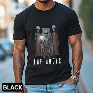 May include: Black t-shirt with a graphic of three grey aliens, one seated on a throne holding a glowing orb. The text "THE GREYS" is below the image. The word "BLACK" is at the bottom.