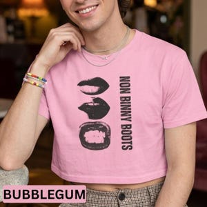Puede incluir: Top corto rosa chicle con un gráfico negro de tres juegos de labios y el texto "NON BINNY BOOTS". La palabra "BUBBLEGUM" está en un rectángulo rosa en la parte inferior.
