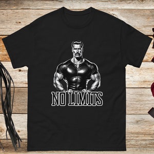 Puede incluir: Camiseta negra con un gráfico de un hombre musculoso con un atuendo de cuero negro. El texto "NO LIMITS" está impreso debajo del gráfico.