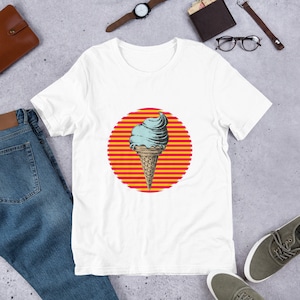 May include: White t-shirt featuring a graphic of an ice cream cone with blue and brown ice cream on a red and yellow striped circle.
