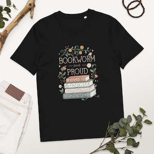 Könnte beinhalten: Schwarzes T-Shirt mit einem grafischen Design eines Stapels Bücher mit floralen Akzenten und dem Text "Bookworm and Proud".