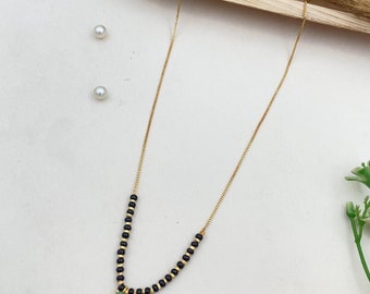 May include: A gold chain necklace with black beads and a light green gemstone pendant.