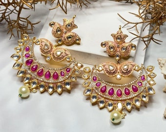 May include: A pair of gold earrings with pink and white enamel, pink and clear stones, and a pearl drop. The earrings are in the shape of a crescent moon.