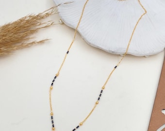 May include: A gold chain necklace with a square-shaped pendant featuring a clear cubic zirconia stone. The chain is accented with black beads.