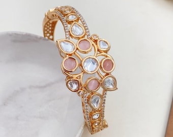 May include: A gold bangle bracelet with a floral design featuring pink and clear stones.