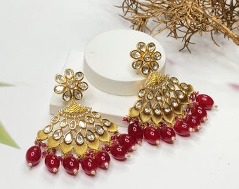 May include: Gold earrings with a floral design and red beads. The earrings are made of metal and have a traditional Indian style.