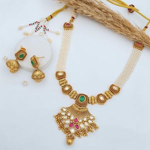 Op de afbeelding: Een gouden ketting met een parelstreng en een hanger met een groen en roze stenen ontwerp. De ketting wordt geleverd met bijpassende oorbellen.