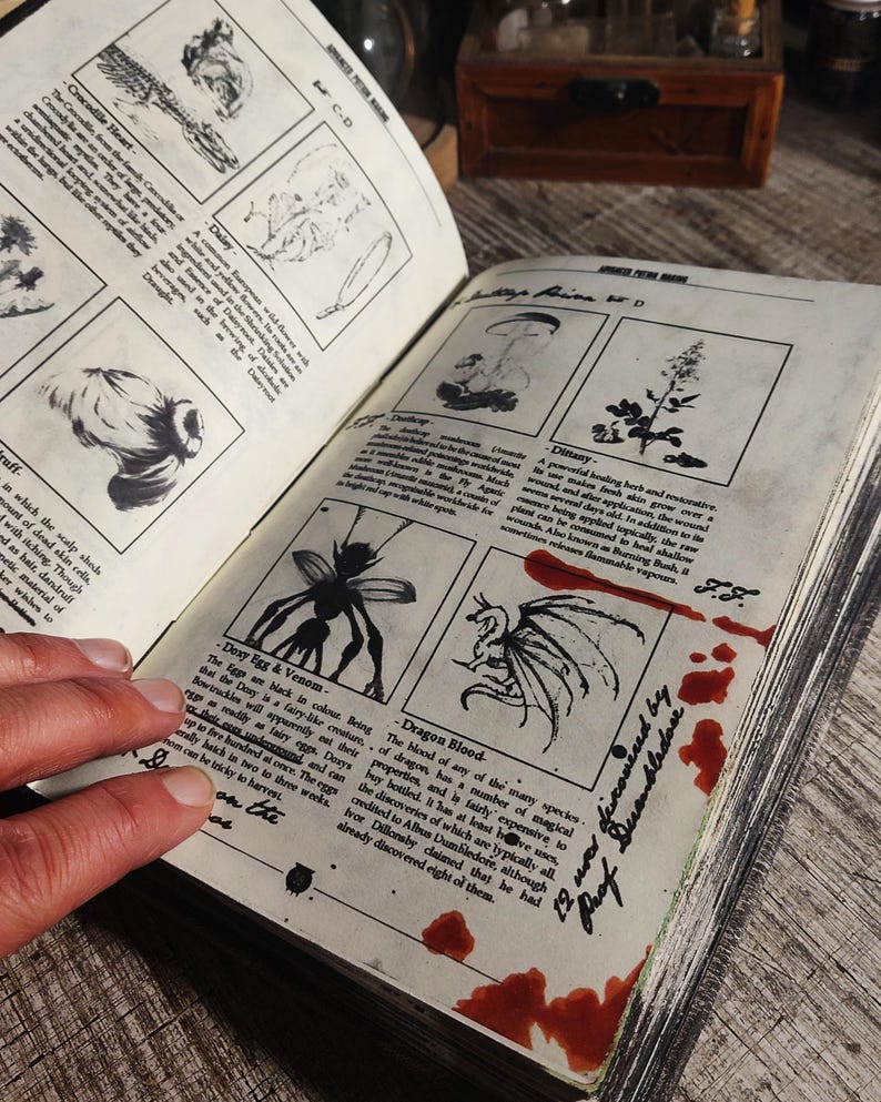 Op de afbeelding: Een vintage boek met illustraties en beschrijvingen van magische ingredi&euml;nten, waaronder Doxy-eieren & gif, drakenbloed en Dimany. Het boek heeft handgeschreven notities en rode vlekken op de pagina's.