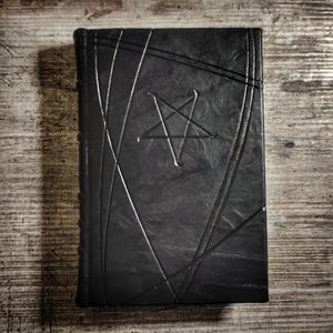 May include: A black leather-bound journal with a pentagram embossed on the front cover.