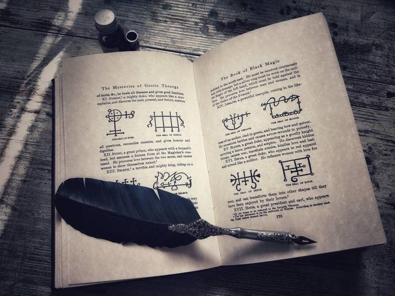 May include: An open book with a black feather quill resting on the pages. The book is titled "The Book of Black Magic" and contains several symbols and text. The book is open to a page with the text "The Mysteries of Gostic Theurgy" and a symbol with the number 18.