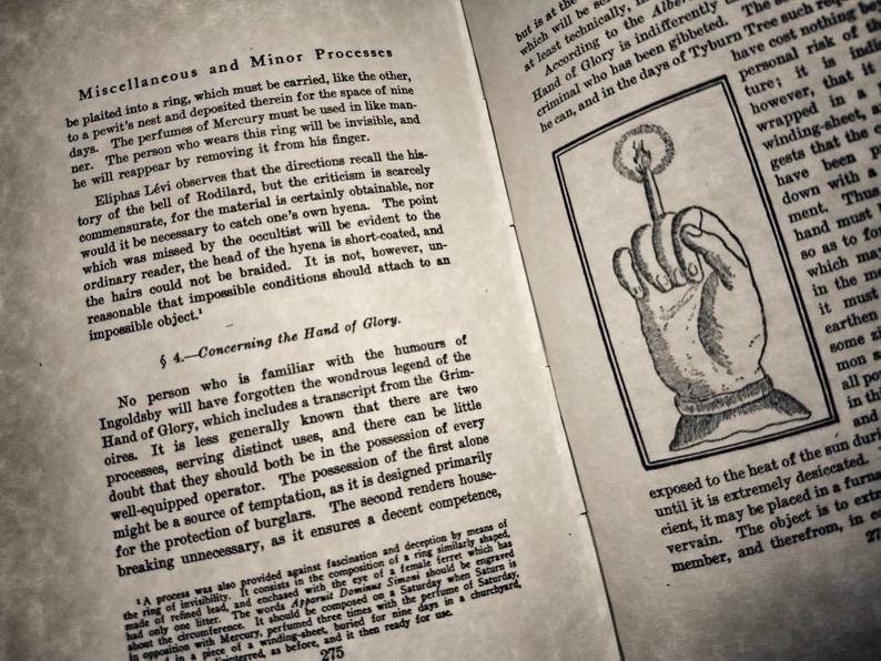 May include: A black and white illustration of a hand holding a lit candle. The hand is depicted with a clenched fist, and the candle is held upright between the thumb and index finger. The image is from an old book and has a vintage aesthetic.