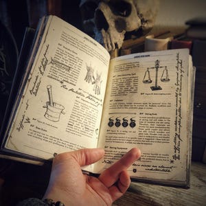 Op de afbeelding: Open boek met illustraties en tekst over het maken van drankjes, weegschalen en andere gereedschappen. Het boek is open op een pagina met de titel "Vuurbeschermingsdrank".