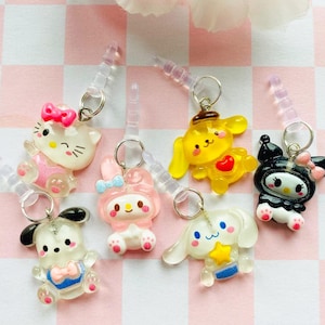 Könnte beinhalten: Eine Sammlung von sieben Handy-Anhängern mit Cartoon-Charakteren. Die Anhänger zeigen verschiedene Charaktere in verschiedenen Farben, darunter eine weiße Katze mit rosa Schleife und ein gelber Hund.