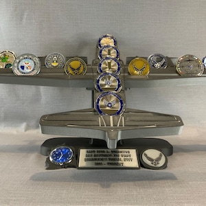 May include: A silver airplane display stand with a blue watch and several silver and gold challenge coins. The stand has a plaque that reads "Capt. David L. Oreintke, USAF Retired. The Way I Remember Things, BTW.  DAD -  "Greenbelt"
