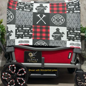 May include: Red and black wagon canopy with a firefighter theme. The canopy is made of fabric and has a patchwork design with images of fire trucks, axes, and fire hydrants. The wagon is red and has black wheels. The text "veer" is visible on the wagon. The text "Shown with Wonderfold poles" is visible below the wagon.
