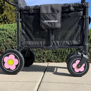 May include: Black Wonderfold wagon with a mesh interior and a black exterior pocket. The wheels are black with a pink flower design and a yellow center. The wagon is on a concrete surface.