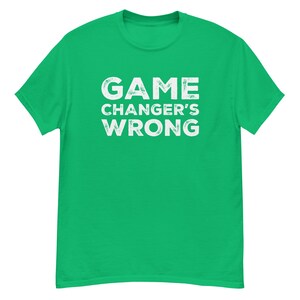Könnte beinhalten: Ein hellgrünes T-Shirt mit dem weißen Text "GAME CHANGER'S WRONG" auf der Vorderseite. Der Text hat ein abgenutztes, strukturiertes Aussehen. Das T-Shirt hat eine einfarbige, leuchtend grüne Farbe.