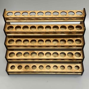 May include: A wooden paint bottle organizer with multiple tiers. Each tier has evenly spaced circular holes designed to hold small paint bottles. The wood has a natural finish with darker edges, creating a layered effect.