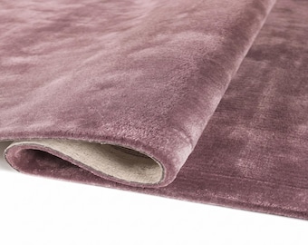 May include: A rolled-up, plush, mauve-colored rug. The rug's soft texture is visible, with a slight sheen. The underside of the rug is a light beige color. The rug is likely made of a soft material, suitable for a living room or bedroom.