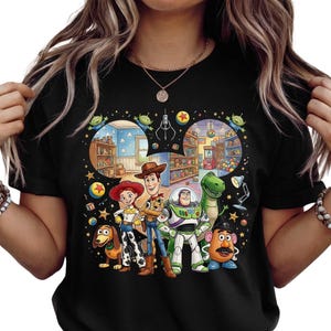 Pode incluir: Camiseta preta com um gr&aacute;fico colorido dos personagens de Toy Story, incluindo Woody, Buzz Lightyear e Rex. O design inclui ilustra&ccedil;&otilde;es de cenas do filme, com um tema divertido e nost&aacute;lgico.