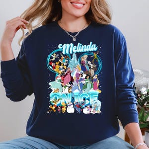 Puede incluir: Una sudadera azul marino con un gr&aacute;fico de personajes de Disney de Frozen y otras pel&iacute;culas de Disney. El texto "Melinda" y "&Eacute;rase una vez" est&aacute; impreso en la sudadera.