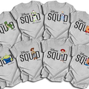 Puede incluir: Una colecci&oacute;n de camisetas grises claras con personajes de Disney. Cada camiseta tiene la palabra "SQUAD" en negrita negra, con el logotipo de Disney arriba. Los personajes incluyen a Buzz Lightyear y Woody.