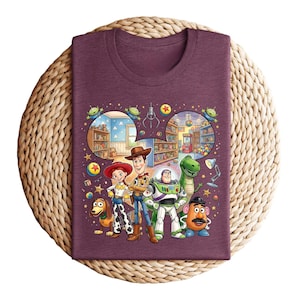 Pode incluir: Uma camiseta bord&ocirc; com um gr&aacute;fico colorido dos personagens de Toy Story. O design apresenta Woody, Buzz Lightyear, Jessie, Rex, Sr. Batata e Slinky Dog, com um fundo de uma loja de brinquedos.