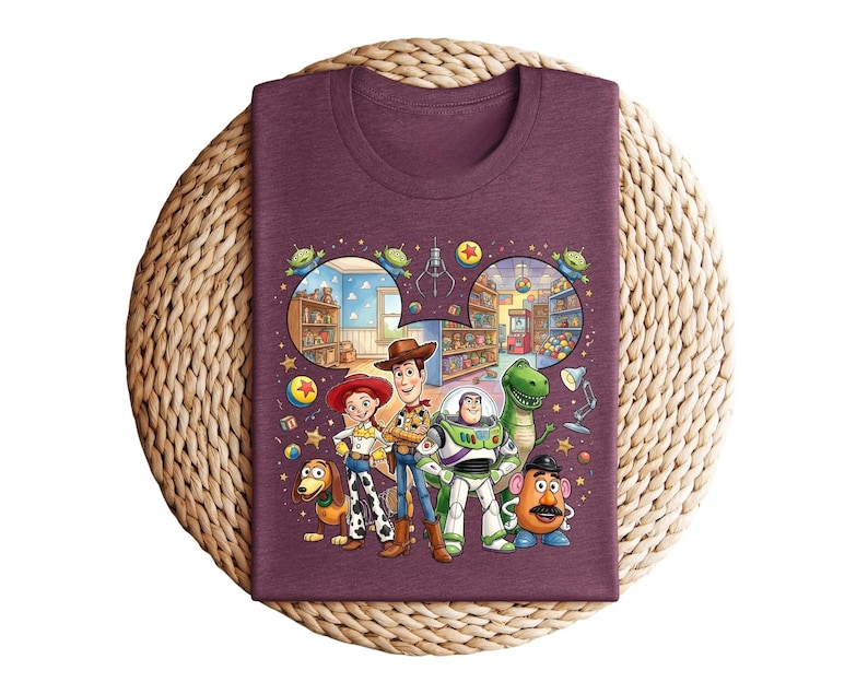 Pode incluir: Uma camiseta bord&ocirc; com um gr&aacute;fico colorido dos personagens de Toy Story. O design apresenta Woody, Buzz Lightyear, Jessie, Rex, Sr. Batata e Slinky Dog, com um fundo de uma loja de brinquedos.