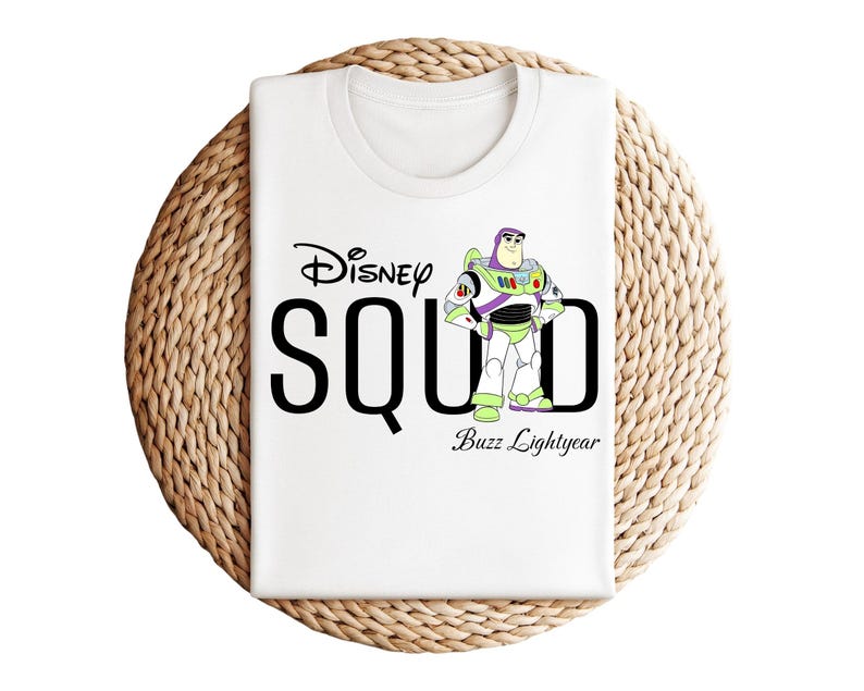 Puede incluir: Camiseta blanca con el texto "Disney SQUAD" en negro y una imagen de dibujos animados de Buzz Lightyear. La camiseta est&aacute; doblada sobre una superficie circular tejida. Las palabras "Buzz Lightyear" est&aacute;n debajo.