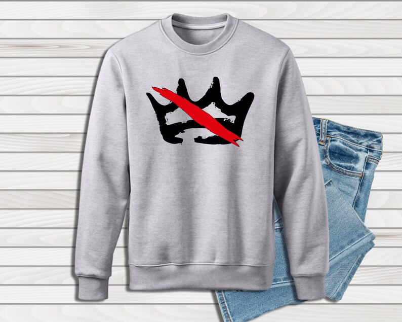 Peut inclure: Un sweat-shirt gris clair avec un motif de couronne noire barr&eacute;e d'une barre rouge. Le sweat-shirt est pr&eacute;sent&eacute; avec un jean en denim bleu. Le motif est centr&eacute; sur le devant.
