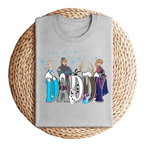 May include: A heather gray t-shirt featuring the word "DADDY" in a stylized font with characters from the movie Frozen. The design includes Elsa, Kristoff, Anna, Olaf, and Sven, with a snowy effect.