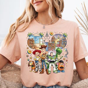 Pode incluir: Camiseta de cor p&ecirc;ssego claro com um gr&aacute;fico colorido de personagens do filme de anima&ccedil;&atilde;o Toy Story. O gr&aacute;fico inclui Woody, Buzz Lightyear, Jessie, Rex, Sr. Cara de Batata e Slinky, com um fundo detalhado.