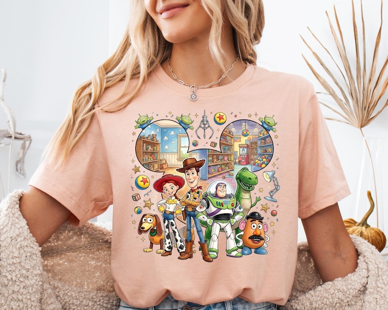Pode incluir: Camiseta de cor p&ecirc;ssego claro com um gr&aacute;fico colorido de personagens do filme de anima&ccedil;&atilde;o Toy Story. O gr&aacute;fico inclui Woody, Buzz Lightyear, Jessie, Rex, Sr. Cara de Batata e Slinky, com um fundo detalhado.