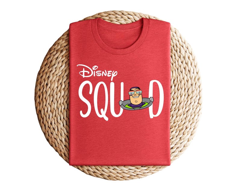 Puede incluir: Camiseta roja con el texto blanco "Disney Squad", con una imagen de dibujos animados de Buzz Lightyear. La camiseta est&aacute; doblada cuidadosamente sobre un salvamanteles circular tejido. La camiseta es de cuello redondo.