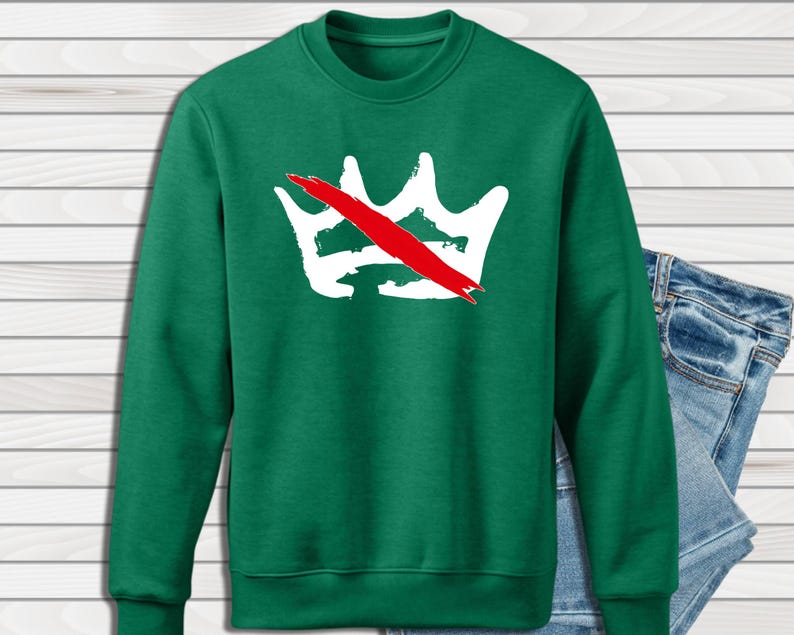 Peut inclure: Un sweat-shirt vert avec un motif de couronne blanche barr&eacute;e d'une bande rouge. Le sweat-shirt est de style col rond et est associ&eacute; &agrave; un jean en denim bleu. Le motif de la couronne est centr&eacute; sur la poitrine.