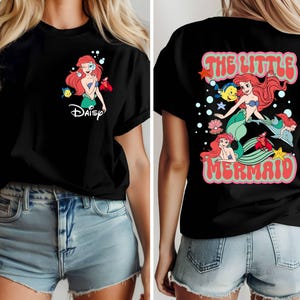 May include: Black t-shirt featuring a colorful graphic of Ariel from The Little Mermaid. The front design includes Ariel and the word "Daisy". The back of the shirt has a larger design with Ariel, Flounder, Sebastian, and the words "The Little Mermaid".